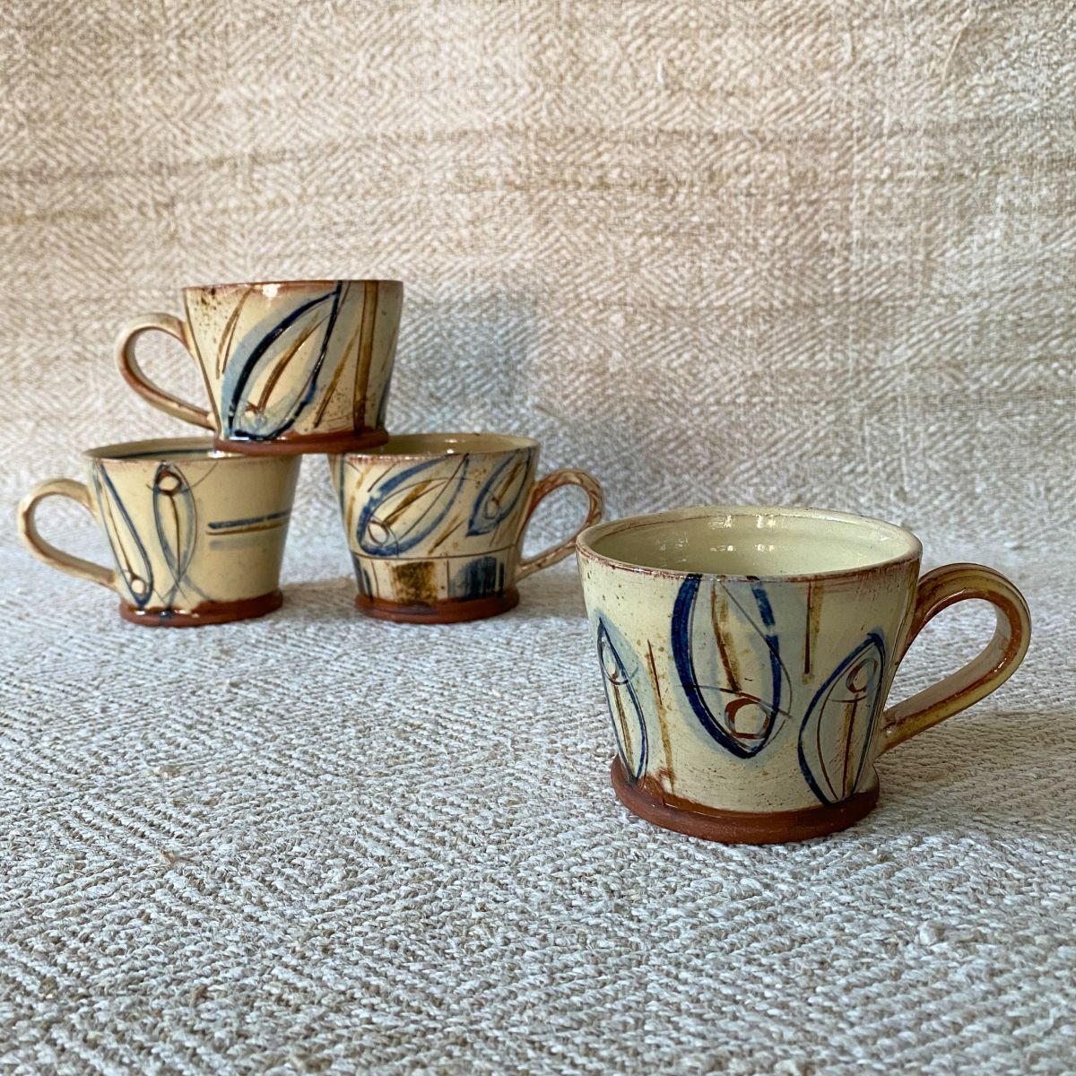 Jennifer Hall stack of slipware glazed espresso mugs on a cream textile background