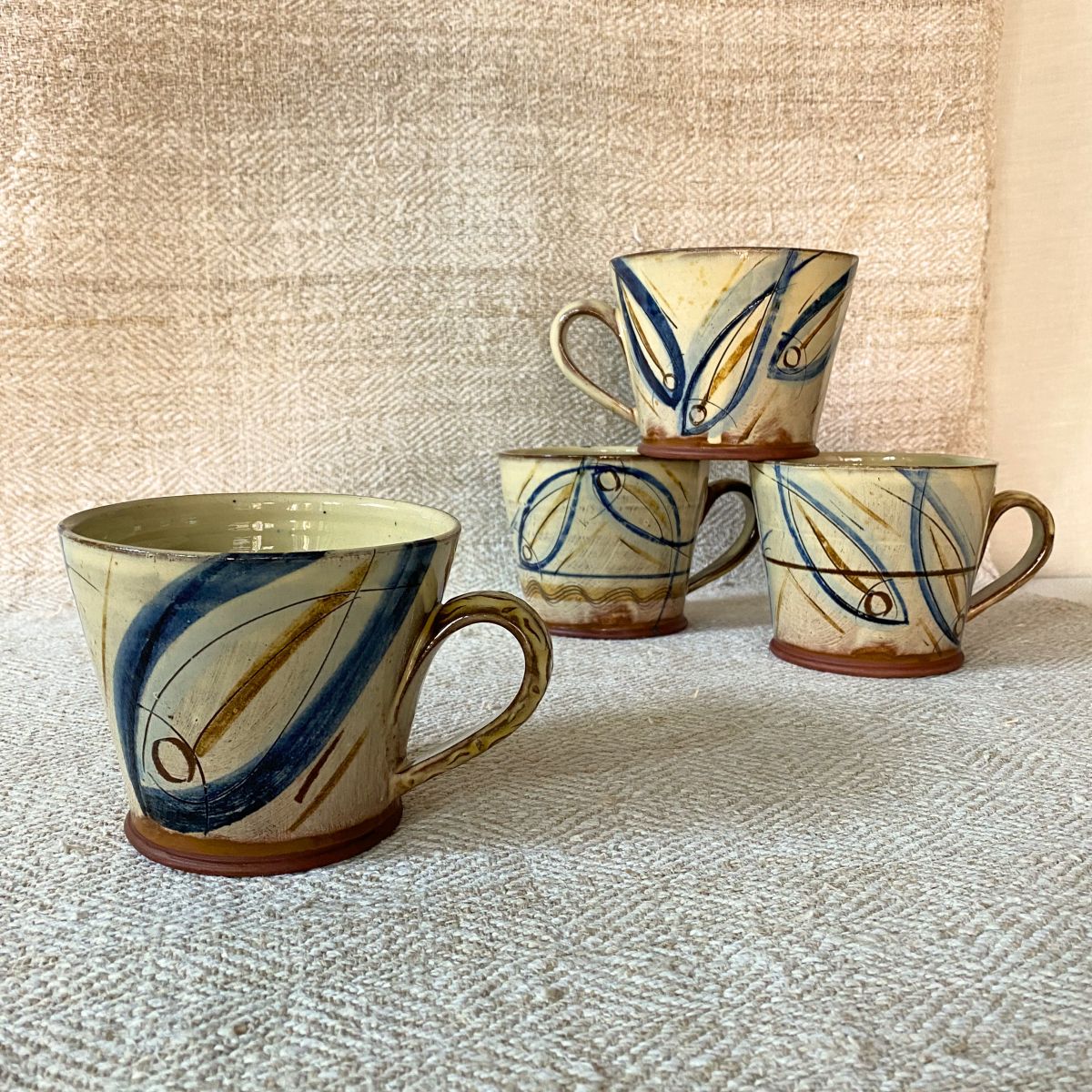 Jennifer Hall Stack of ceramic mugs on cream textile backdrop
