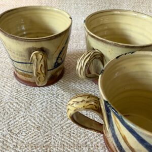 Jennifer Hall handle detail of three slipware mugs on cream textile backdrop