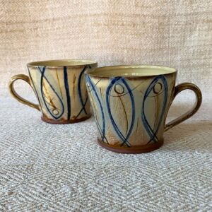Jennifer Hall pair of slipware glazed tea mugs on a cream textile background