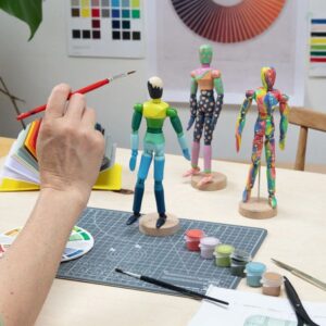 Three Paint & Pose Mannequins being painted in rainbow colours, posed on a table