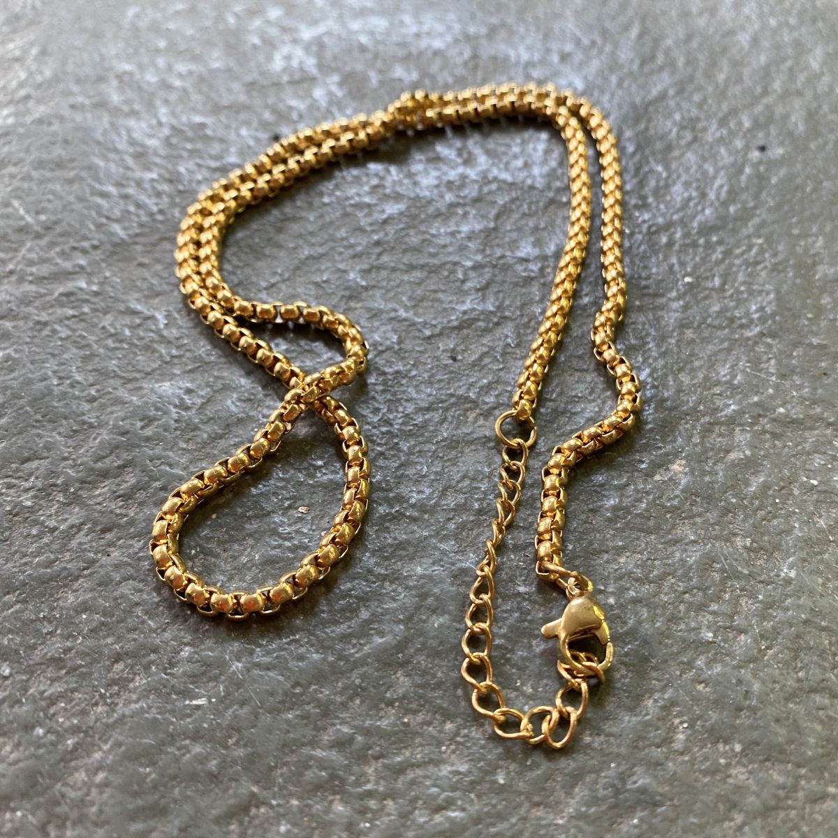Gold box chain on a grey stone tile
